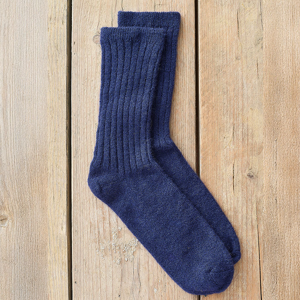 A pair of dark navy blue ribbed knit crew socks laid flat on a light brown wooden plank surface.