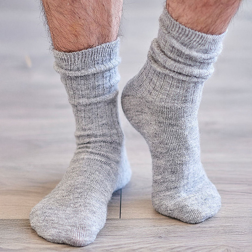 A close-up of a person's feet wearing light gray ribbed crew socks on a light wood floor.