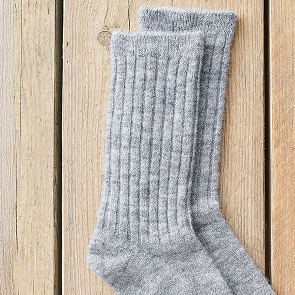 A pair of light gray ribbed knit crew socks displayed on a light wood plank surface.