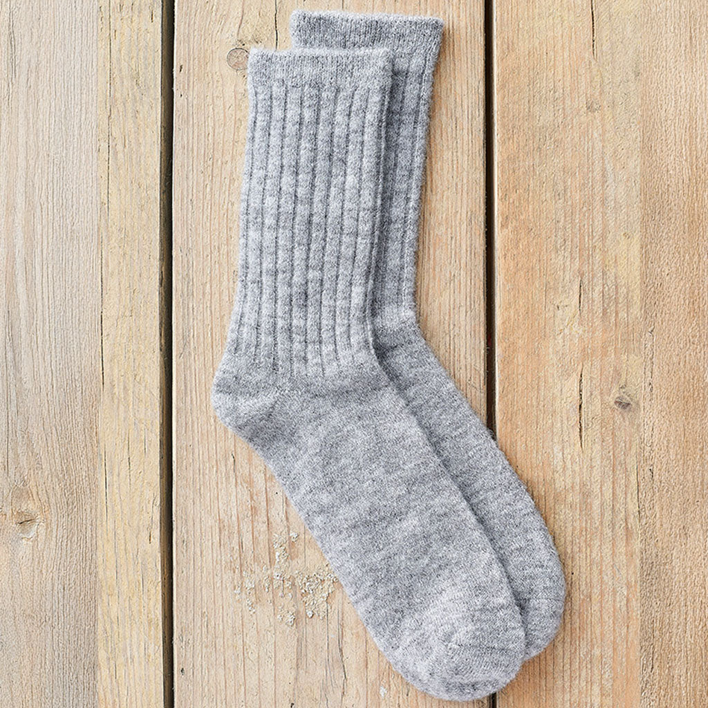 A pair of light gray ribbed crew socks laid flat on a light wood plank background.