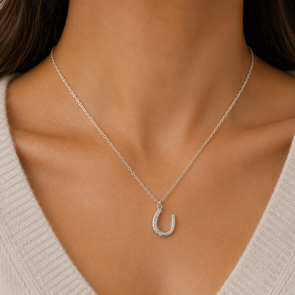 A close-up of a model wearing a delicate silver chain necklace with a crescent-shaped pendant studded with small clear crystals, paired with a light beige knit top.