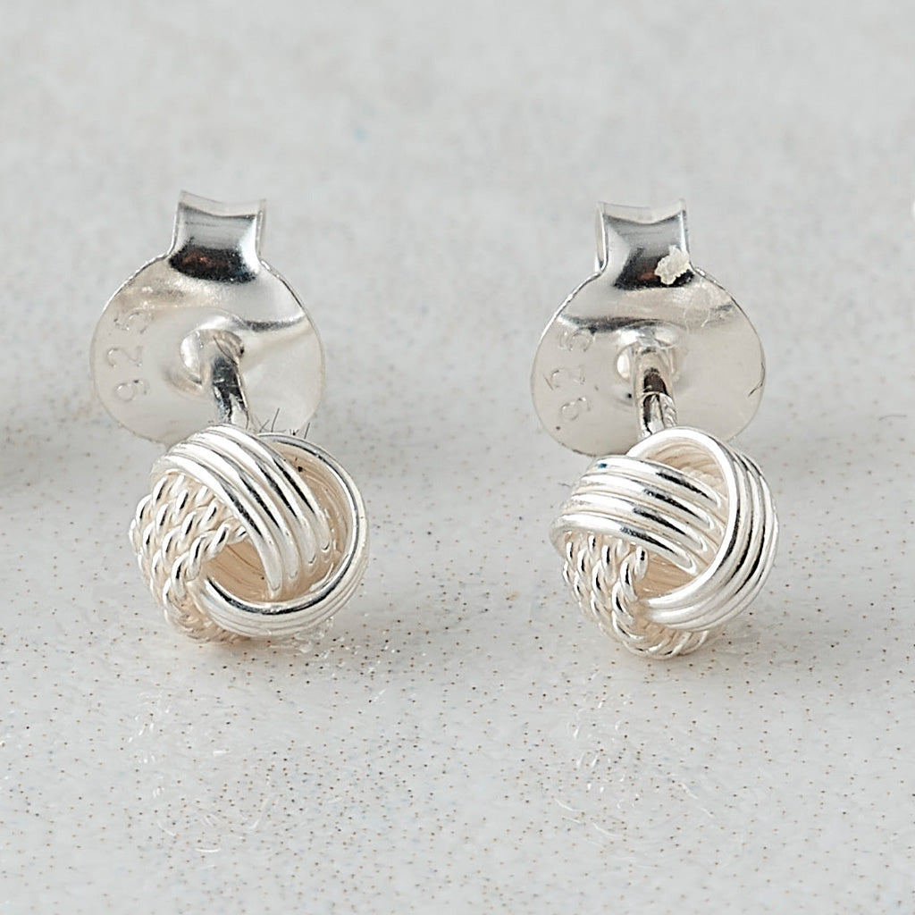A pair of sterling silver knot stud earrings with flat back posts, displayed on a light gray textured surface.