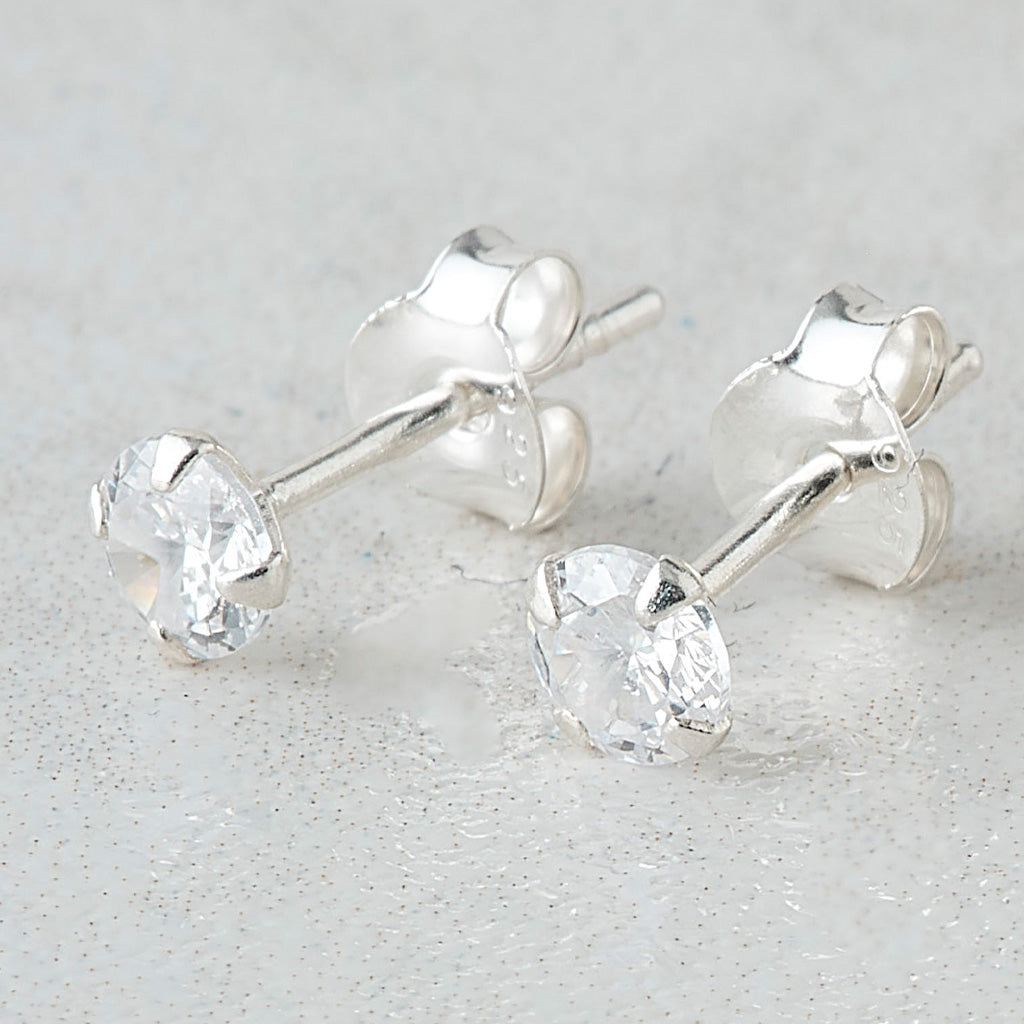 A pair of silver stud earrings with clear faceted round-cut gemstones, shown on a light gray textured background.