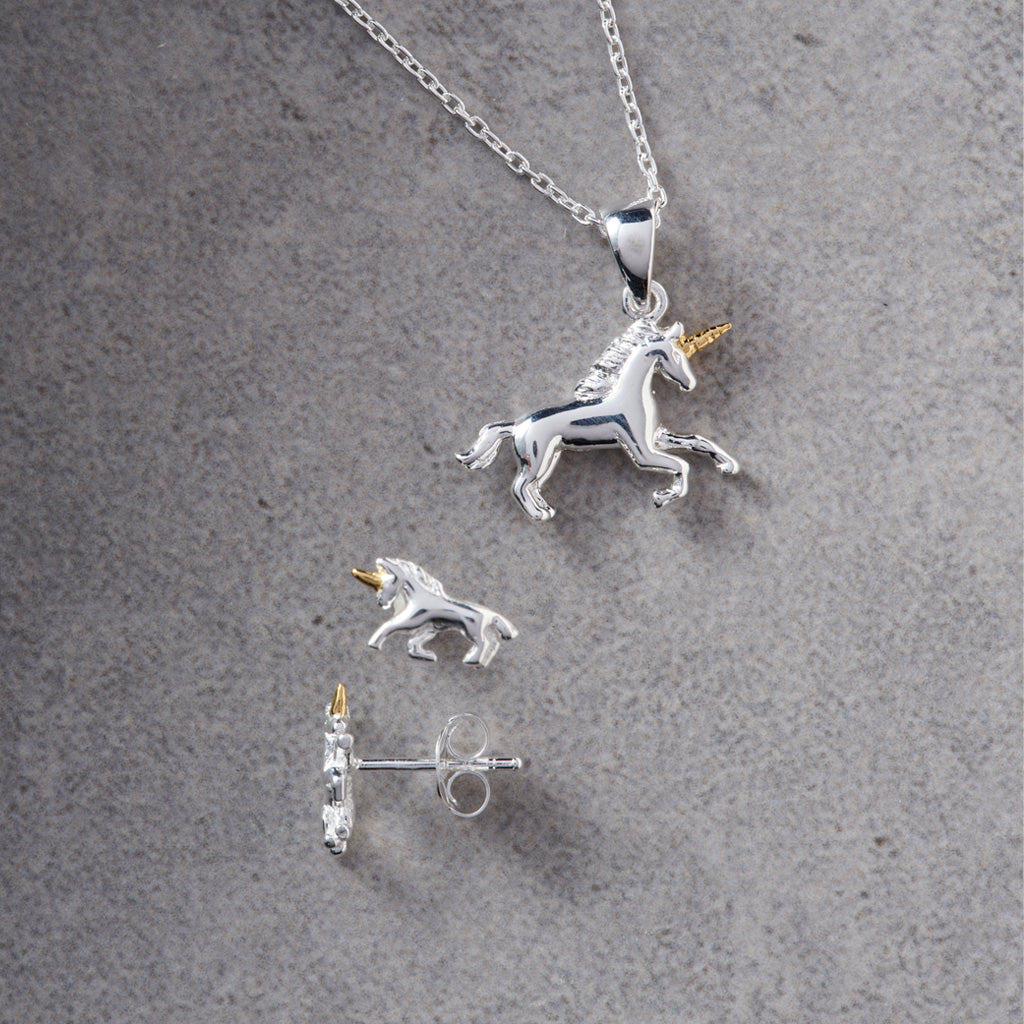 A silver unicorn pendant necklace with a matching stud earring, displayed on a textured gray background. The unicorn pendants feature polished silver bodies with small gold accents on the horns.
