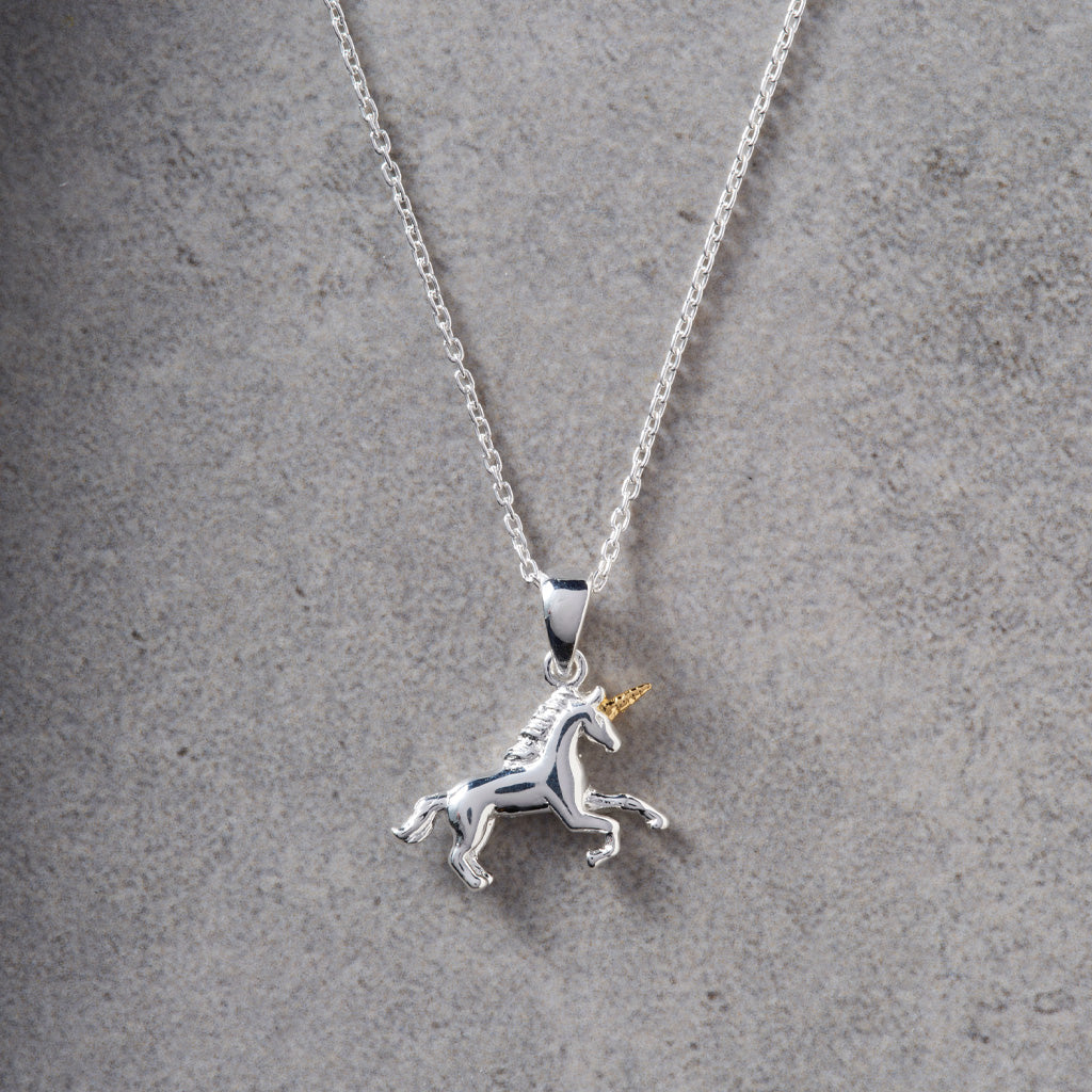 A sterling silver unicorn pendant necklace with a gold horn, hanging from a silver chain against a textured gray background.