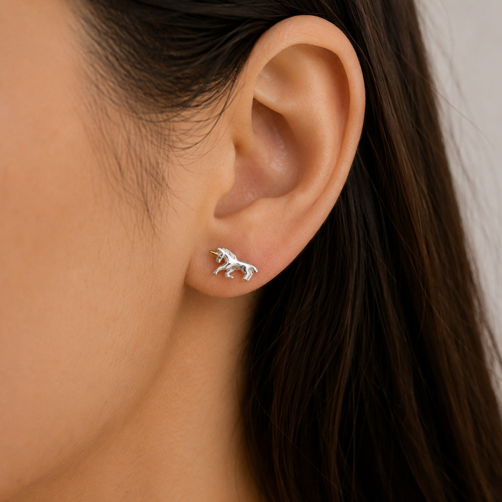 A close-up of a person's ear wearing a small silver stud earring shaped like a horse, with dark brown hair against a light neutral background.