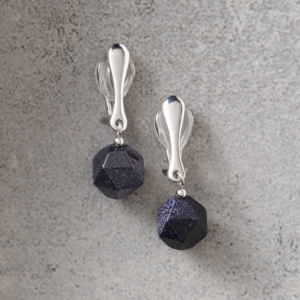 A pair of silver-toned drop earrings with faceted dark blue-gray beads, displayed on a textured gray surface.