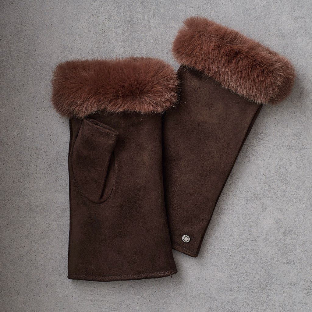 A pair of dark brown suede gloves with thick, fluffy brown fur trim at the cuffs, laid flat on a textured gray background.