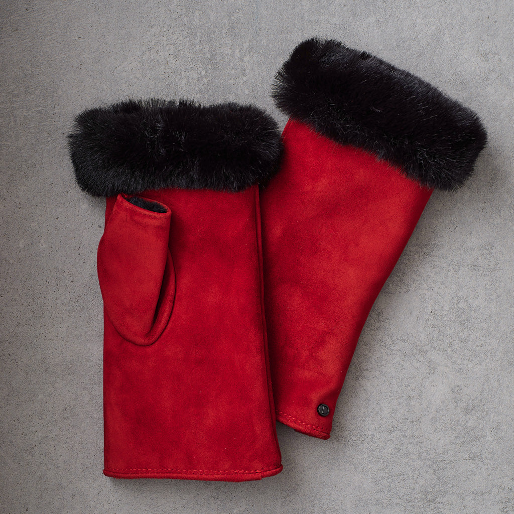 A pair of red suede winter gloves with black fur trim at the cuffs, laid flat on a textured gray background.