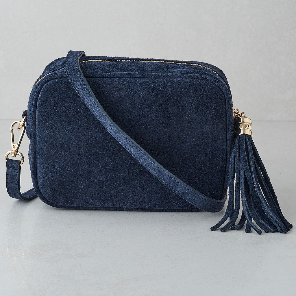 A navy blue suede crossbody bag with a matching tassel detail and gold-tone hardware, displayed on a light gray background.