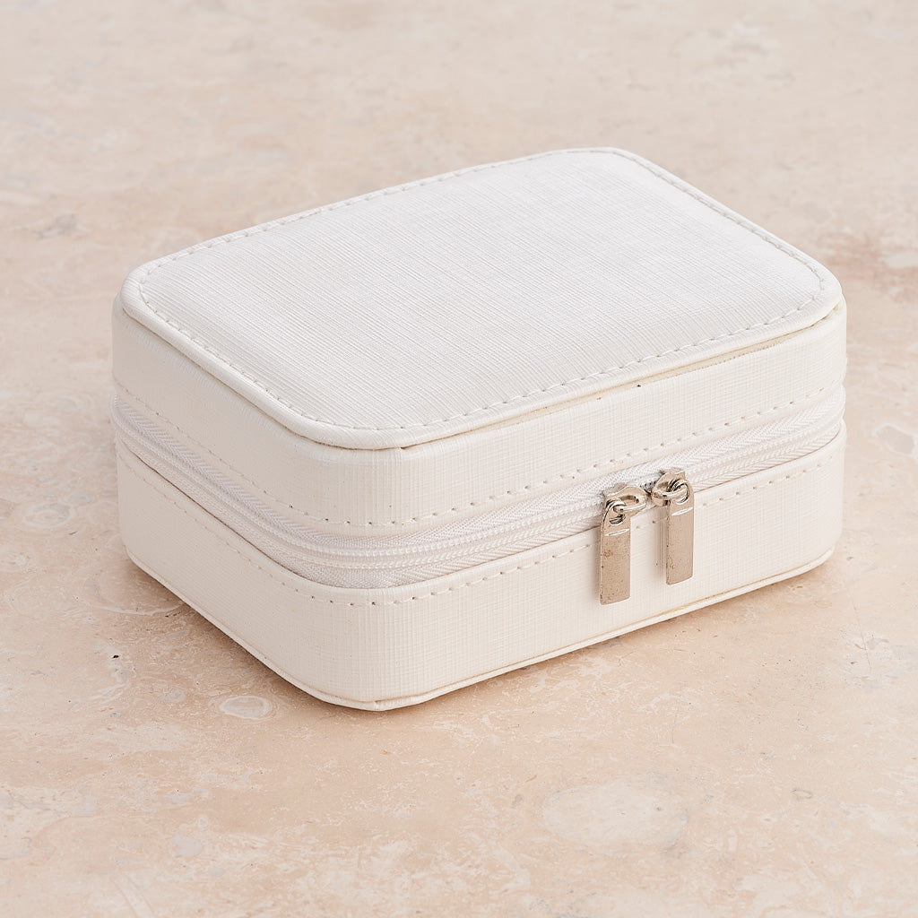 A small rectangular white faux-leather jewelry box with a double zipper and silver-tone pull tabs, photographed on a light beige stone-like surface.