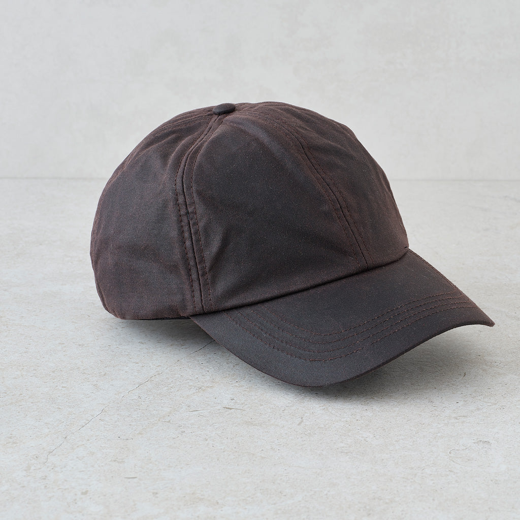 A dark brown baseball cap with a curved brim, photographed from a side angle on a light gray textured background.