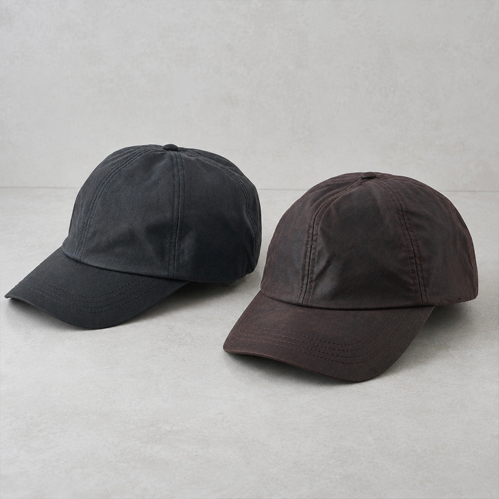 Two classic six-panel baseball caps on a light gray textured background. The cap on the left is washed black, and the cap on the right is washed dark brown.