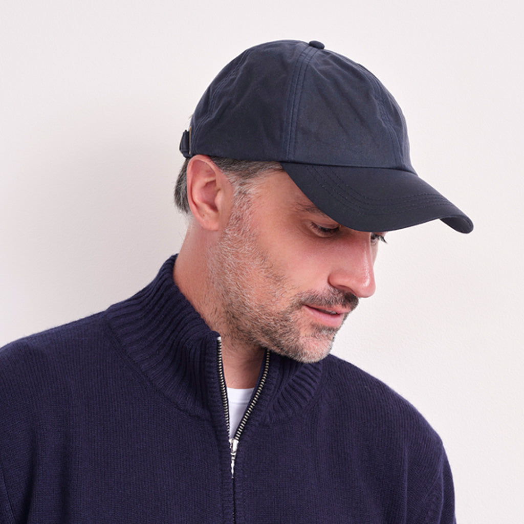 A man wearing a dark navy blue baseball cap and a matching navy blue zip-up sweater, shown in a close-up profile against a plain light background.
