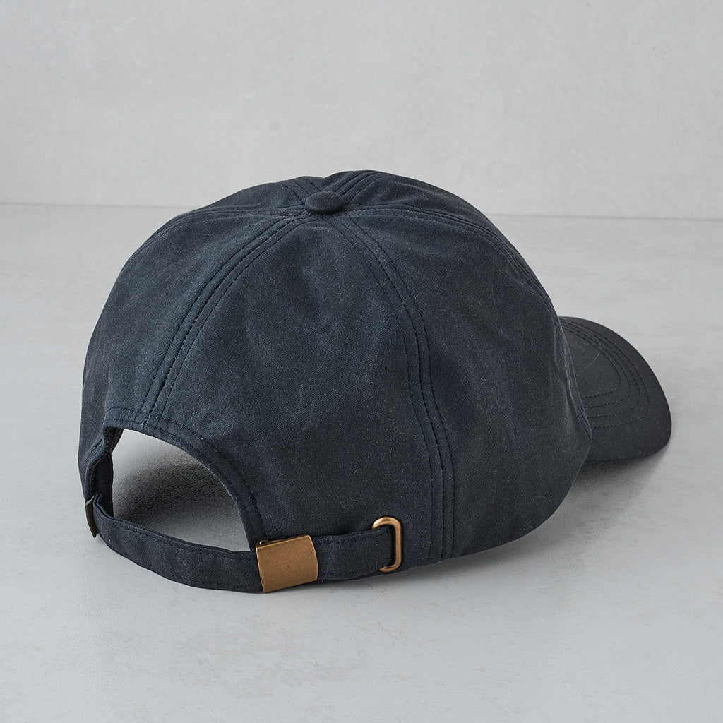 A dark navy blue cotton baseball cap shown from the back, featuring a matching fabric strap with a gold-tone metal buckle and a small tan leather accent.