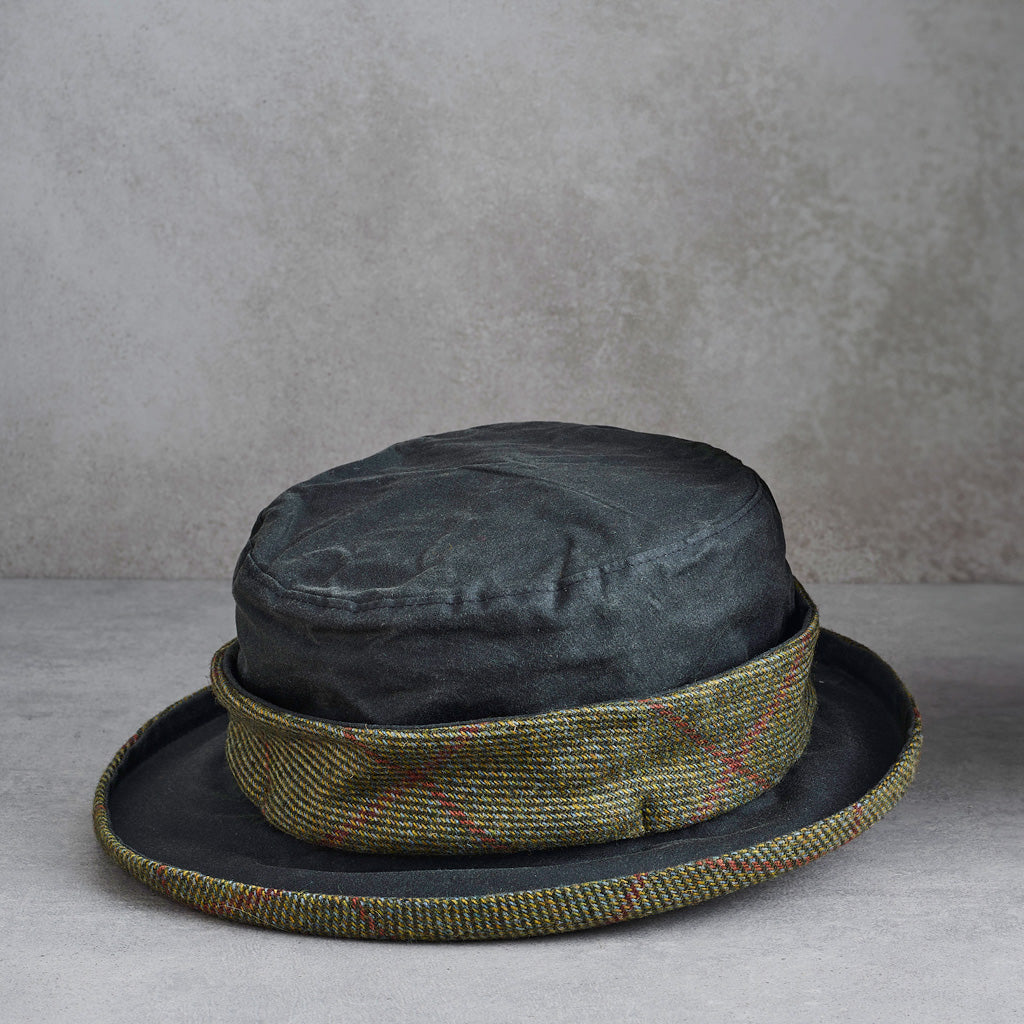 A dark charcoal gray felt hat with a textured olive green and red tweed band, displayed on a neutral gray surface against a textured gray background.