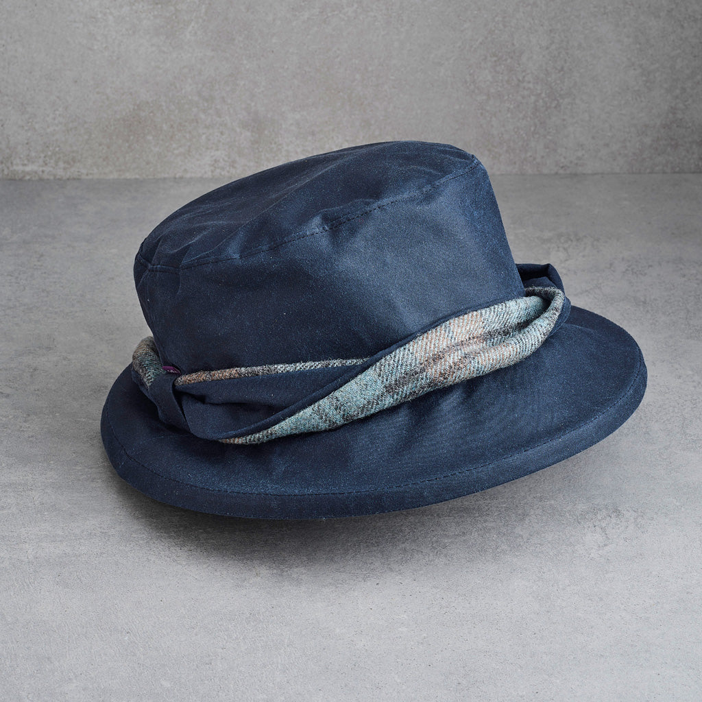A navy blue fedora hat with a textured woven band in a light blue, gray, and white pattern, displayed on a gray concrete surface.