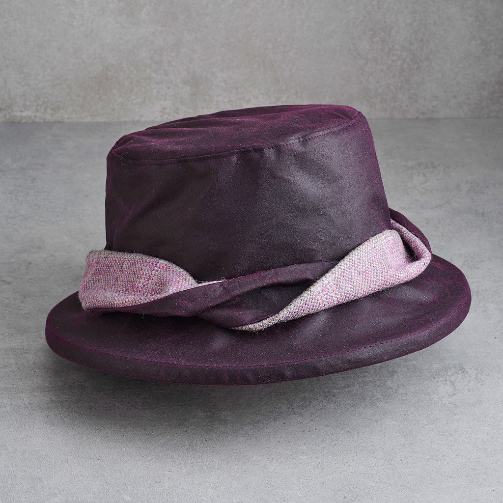 A dark purple fedora hat with a textured light pink band, displayed on a neutral gray surface.