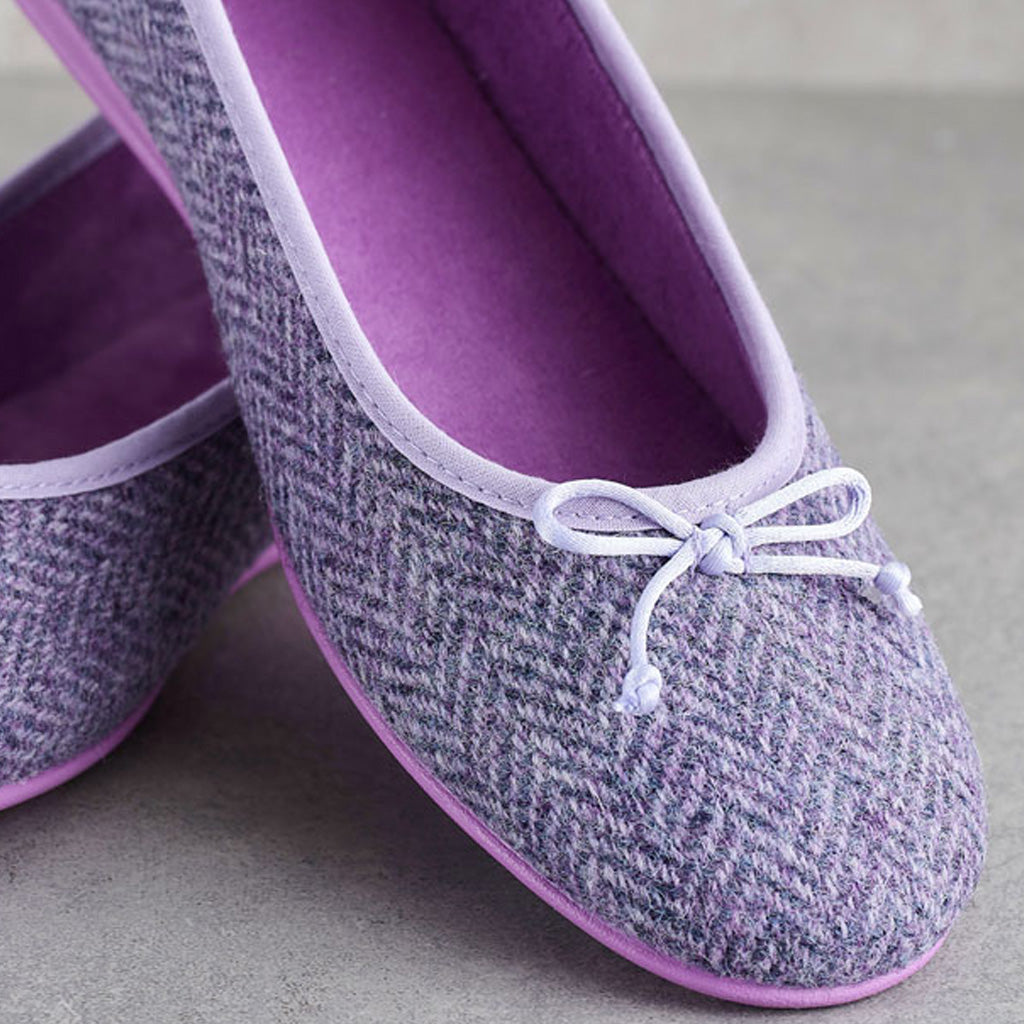 A pair of women's slip-on shoes in a gray and purple herringbone pattern, featuring a light purple interior and a small white bow on the toe.