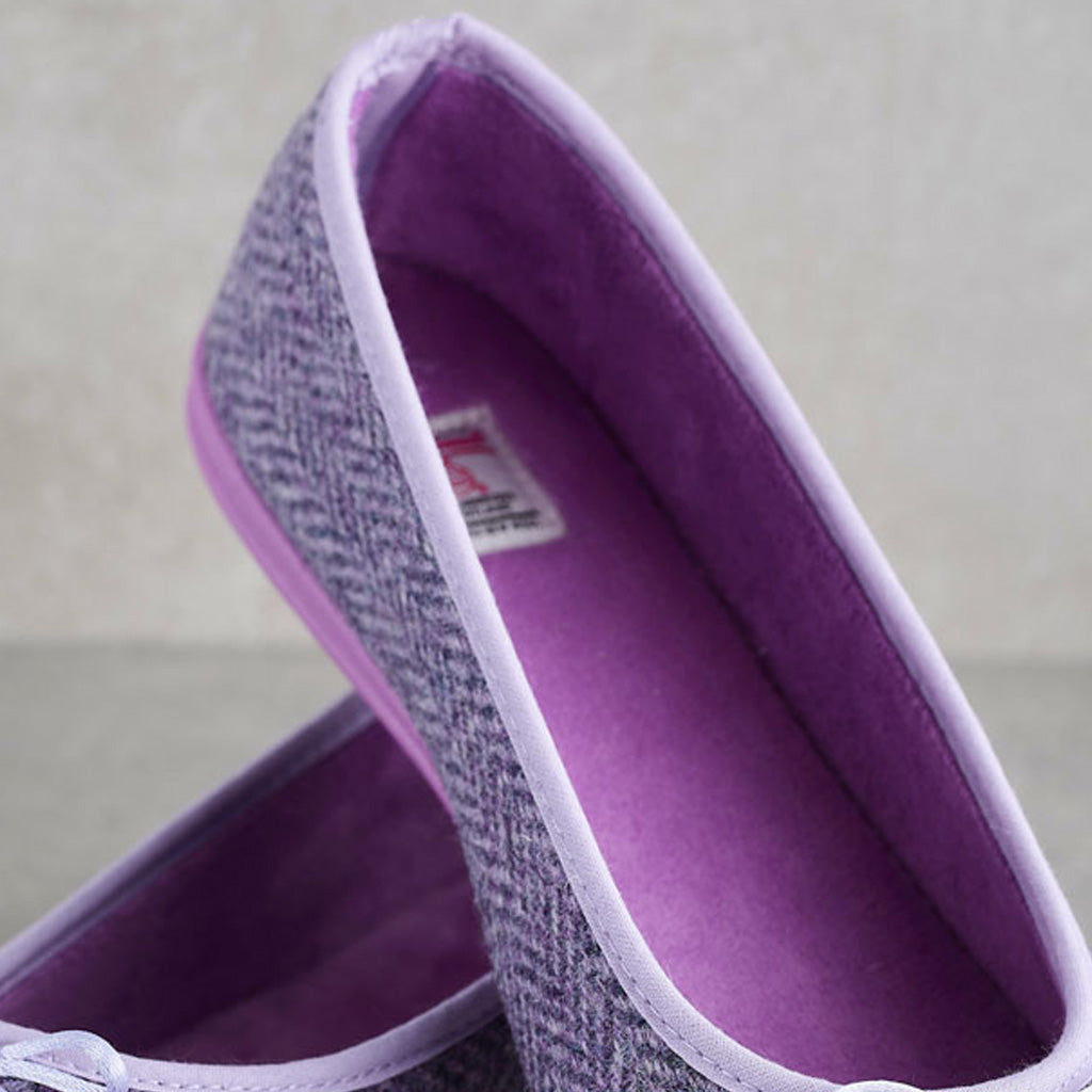 A close-up of a purple and gray herringbone slip-on shoe with a solid purple interior and a light purple trim, resting on another shoe against a neutral background.