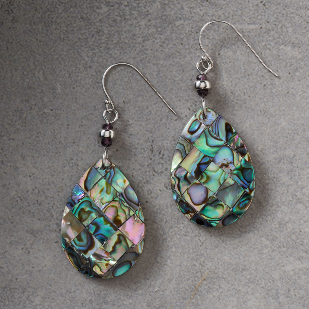 A pair of teardrop-shaped dangle earrings featuring a mosaic of iridescent abalone shell pieces in shades of green, blue, pink, and gold, suspended from silver fishhook wires with small dark beads.