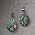 A pair of teardrop-shaped dangle earrings featuring a mosaic of iridescent abalone shell pieces in shades of green, blue, pink, and gold, suspended from silver fishhook wires with small dark beads.