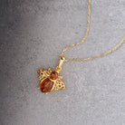 A gold-tone bumblebee pendant necklace with amber-colored gemstone accents, displayed on a textured gray background.