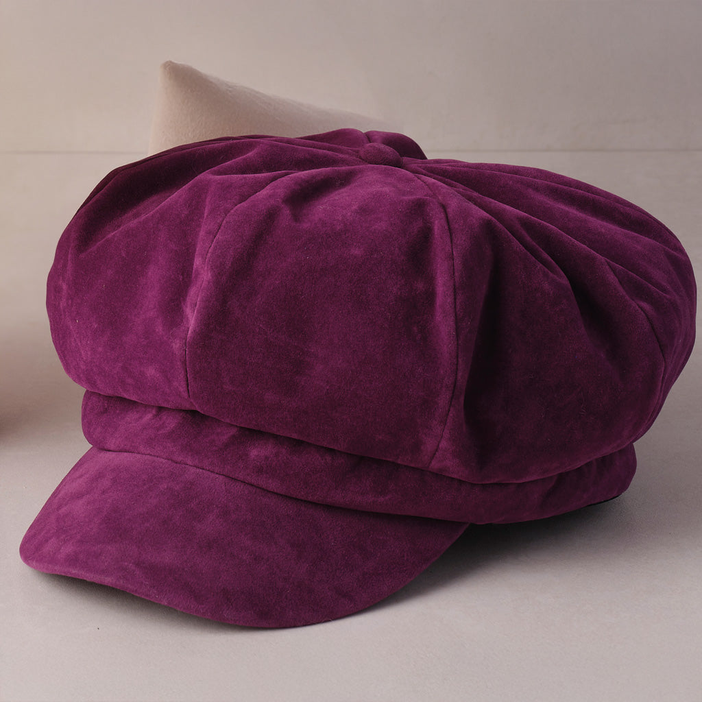 A deep purple velvet newsboy cap with a rounded crown and short brim, photographed on a neutral light gray background.