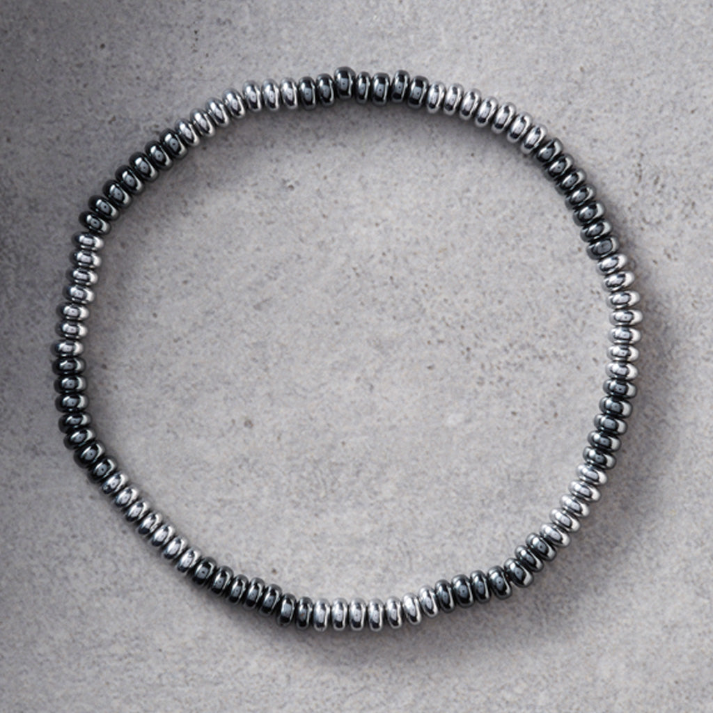 A beaded stretch bracelet made of small metallic silver beads, arranged in a circular shape on a textured gray background.