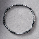 A beaded stretch bracelet made of small metallic silver beads, arranged in a circular shape on a textured gray background.