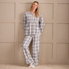 A woman wearing a long-sleeve plaid pyjama top in cream, white, and navy blue, standing against a beige paneled wall.