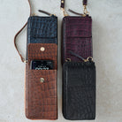 Three vertical phone wallet cases with a crocodile-embossed texture, shown side by side on a light gray surface. From top to bottom, the colors are dark blue, brown, and black.
