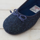 A close-up of a dark navy blue knit slipper with a matching fabric bow on the toe, resting on a light-colored wooden surface.