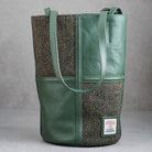 A green leather and herringbone tweed bucket bag with dual shoulder straps and a visible Woolworths label patch on the lower front, photographed against a neutral gray background.