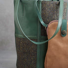 A green leather and herringbone tweed bucket bag with dual shoulder straps and a visible Woolworths label patch on the lower front, photographed against a neutral gray background.