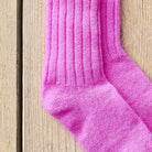 A close-up of a bright pink ribbed knit sock laid on a light wood plank surface.