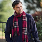 A man wearing a navy blue sweater and a red and black plaid scarf, photographed outdoors with a blurred green background.
