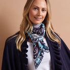 A woman wearing a navy blue and turquoise paisley scarf with white accents, styled around her neck over a white top and a dark navy cardigan.