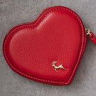 A red heart-shaped leather coin purse with a gold deer logo on the front, photographed on a textured gray background.