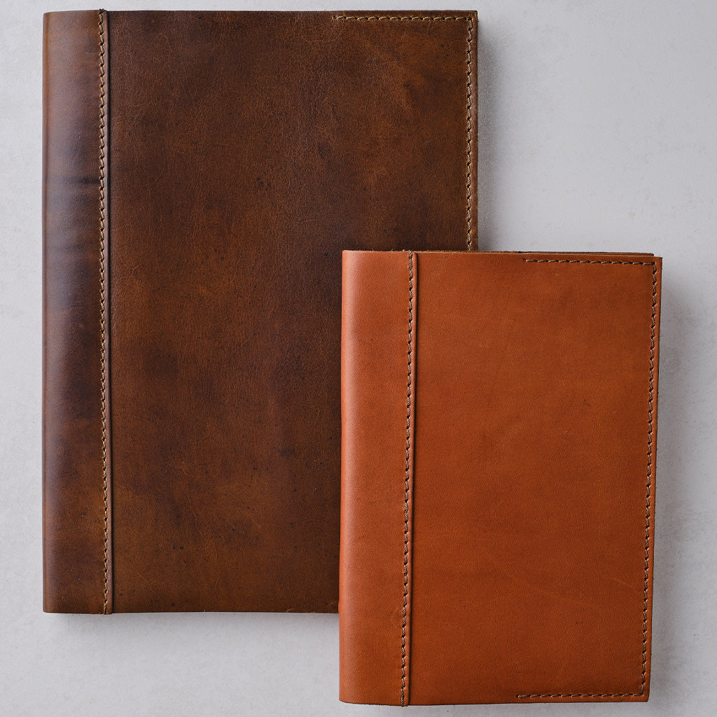 Two leather notebook covers in different brown shades, one dark brown and one tan/cognac, displayed on a light gray background.