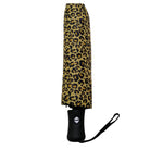 A closed compact umbrella with a tan and black leopard print pattern, featuring a black handle and wrist strap, shown against a plain white background.