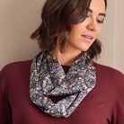 A woman wearing a dark paisley-patterned infinity scarf over a burgundy top, photographed against a plain beige wall.