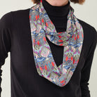 A multicolor abstract patterned scarf with red, blue, green, and purple swirls, worn as a loop necklace over a black turtleneck sweater.