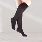A pair of sheer black knee-high socks worn on a model's legs, shown floating against a light gray studio background.