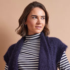 A woman wearing a navy blue fuzzy sleeveless cardigan over a black and white striped turtleneck, set against a solid beige background.