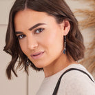 A woman with short brown hair wearing silver-toned drop earrings with dark blue crescent moon charms, photographed in a softly lit indoor setting.