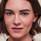 Close-up portrait of a woman wearing a small silver and black drop earring, with her face filling the frame against a soft light background.