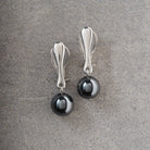 A pair of silver-toned drop earrings with polished oval posts and dark metallic spherical charms, displayed on a textured gray surface.