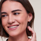 Close-up of a smiling woman wearing a small silver hoop earring with a single white pearl, against a soft beige background.