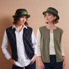 Two women wearing a white button-down shirt and one wearing a dark navy vest with a green argyle pattern, posed against a solid beige background. and the other women wearing sage green argyle pattern waistcoat.